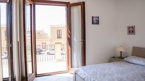 Un dormitorio con cama, mesita de noche, lámpara y vistas al exterior por una puerta abierta.