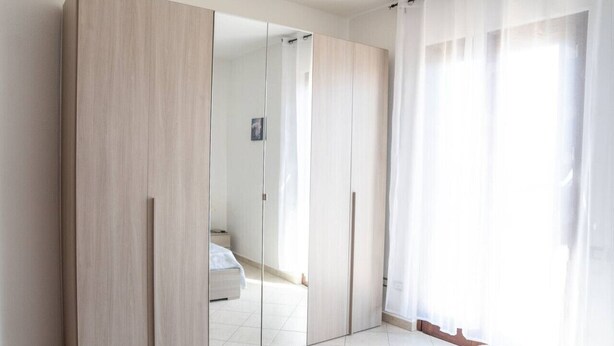 Un dormitorio con un armario grande, una cama y una ventana con cortinas traslúcidas.