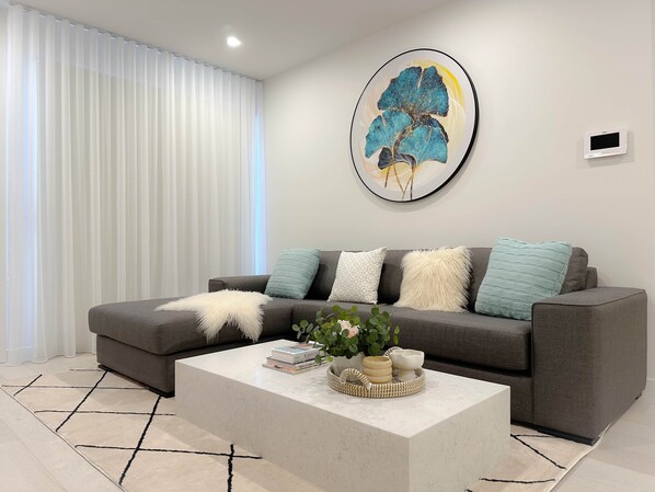 A modern living room with a grey sofa, a white coffee table, and a large abstract painting on the wall.