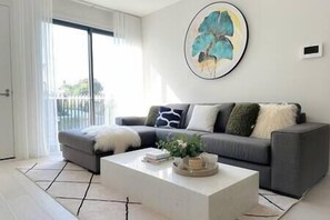 A modern living room with a grey sofa, a white coffee table, and a large abstract painting on the wall.