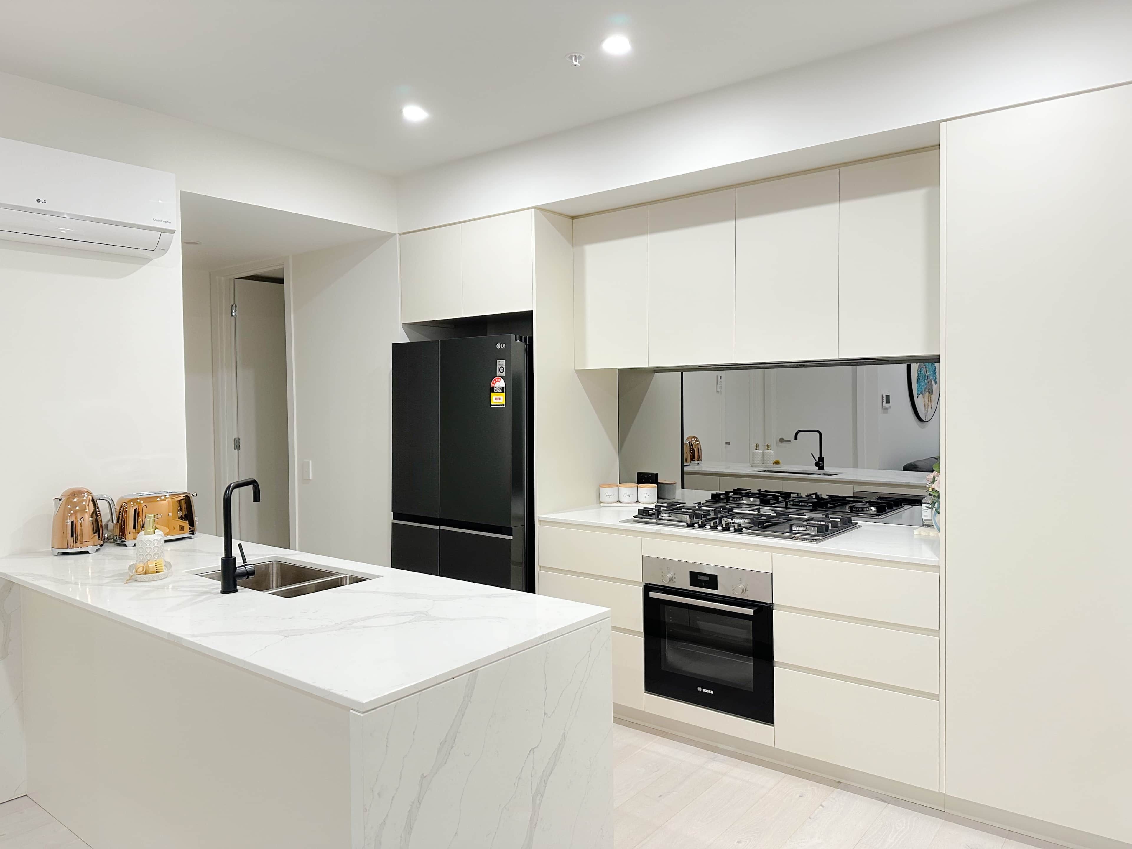A modern kitchen with a marble island, black refrigerator, Bosch oven, and stainless steel appliances.