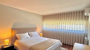 A bedroom with a bed, bedside lamps, a window with blinds, and a radiator.