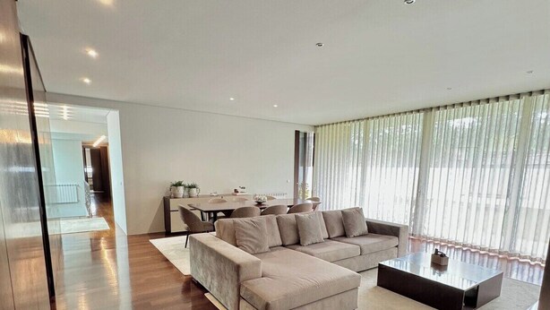 Een moderne woonkamer met een hoekbank, een salontafel en een eethoek op de achtergrond.