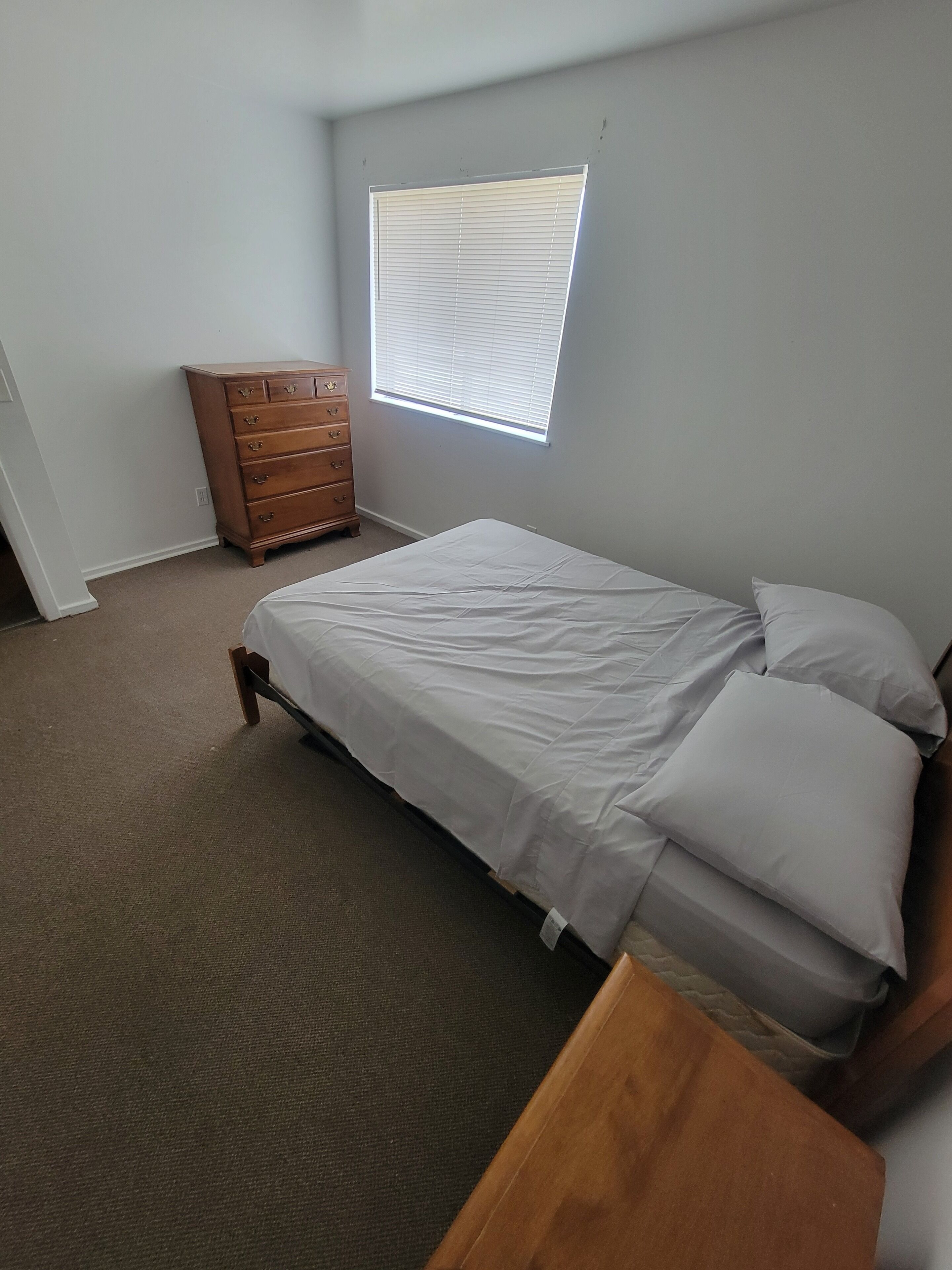 A bedroom with a bed, a dresser, and a window with blinds.