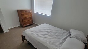 Een slaapkamer met een bed, een dressoir en een raam met jaloezieën.