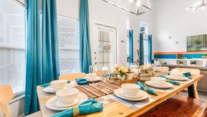 Een eetruimte met een houten tafel voor vier personen, blauwe gordijnen en een moderne kroonluchter.