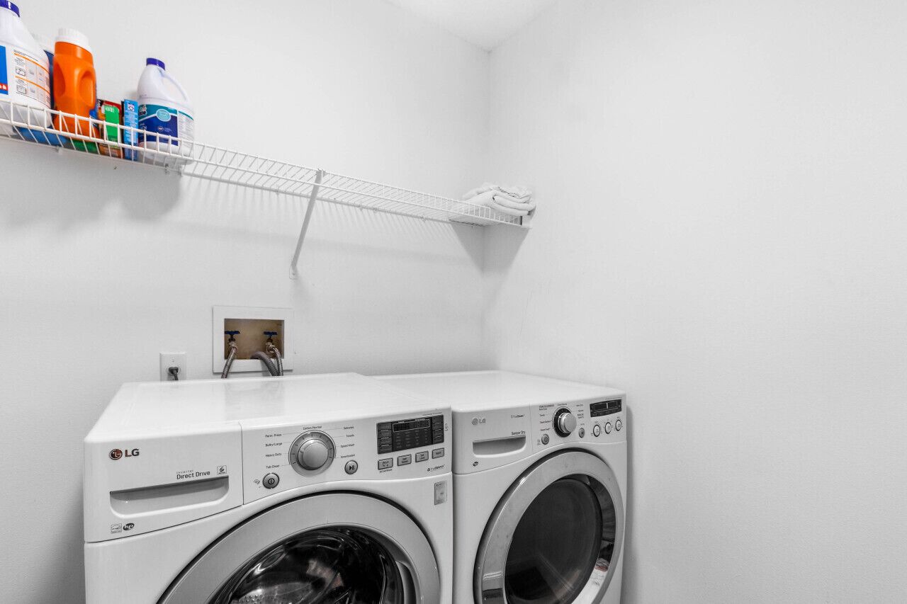 Zona de lavandería con dos lavadoras LG Direct Drive, un estante con botellas de detergente y un tendedero.
