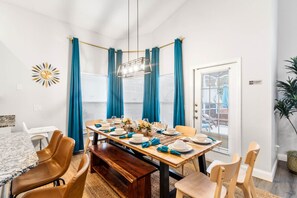Un coin repas avec une table en bois dressée pour quatre personnes, des rideaux bleus et un lustre moderne.
