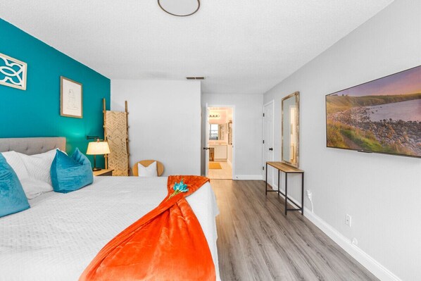 A bedroom with a bed, a bedside table, a lamp, a wall-mounted mirror, and a painting.