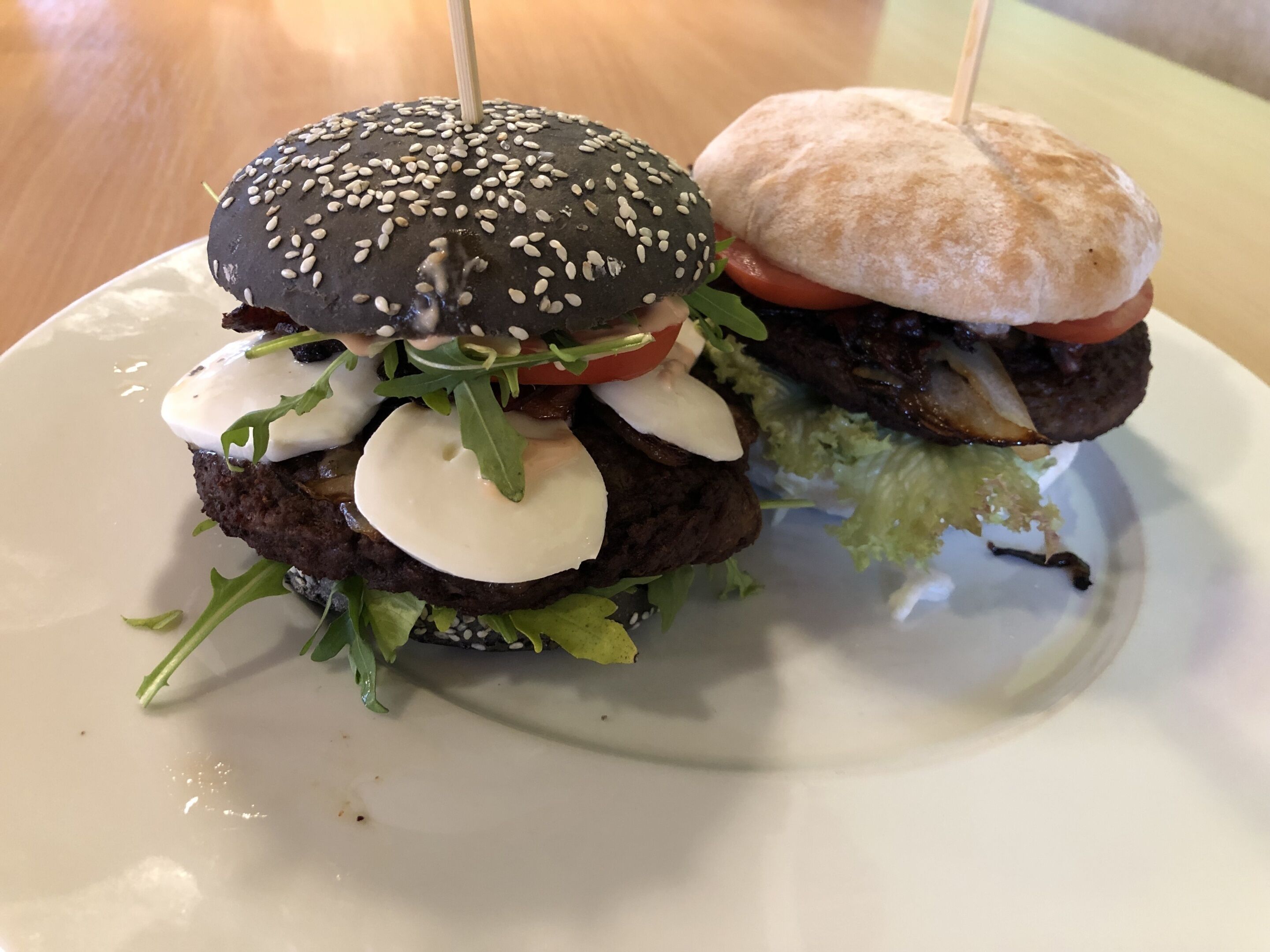 Una hamburguesa con pan de sésamo y una porción de pan plano sobre un plato blanco.