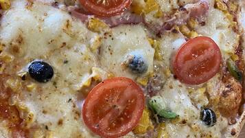 Una pizza con tomates, aceitunas y maíz sobre una superficie de madera.