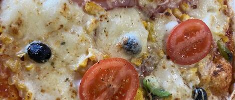 A pizza with tomatoes, olives, and corn on a wooden surface.