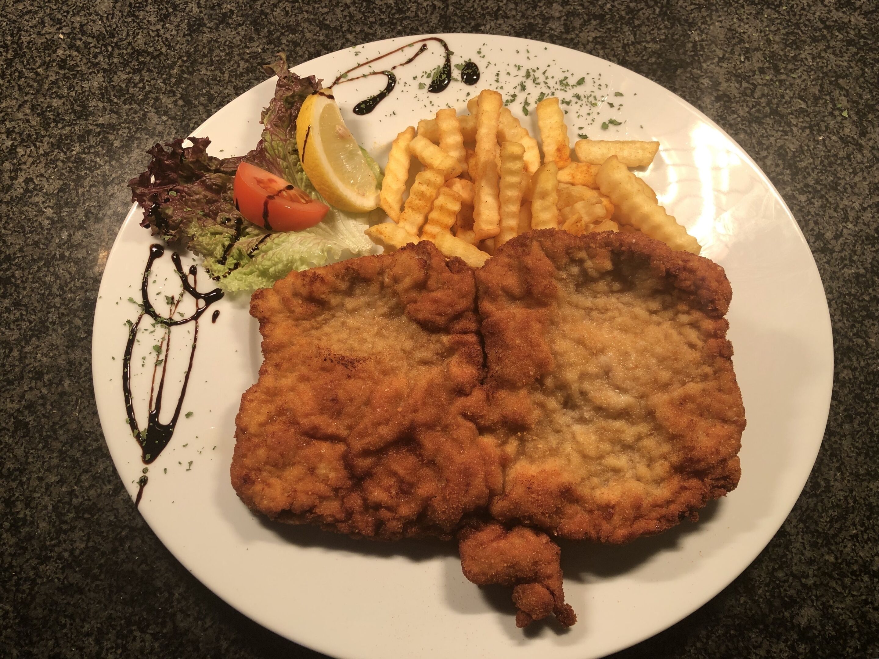 A plate with a breaded and fried cutlet, French fries, a side salad, and a lemon wedge.