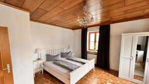 A bedroom with a wooden ceiling, a bed with grey bedding, a white wardrobe, and a window with curtains. - Gasthof & Pension Zum Zacherwirt (Hengersberg)