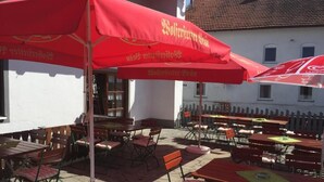 An outdoor seating area with red umbrellas and wooden tables and chairs. - Gasthof & Pension Zum Zacherwirt (Hengersberg)