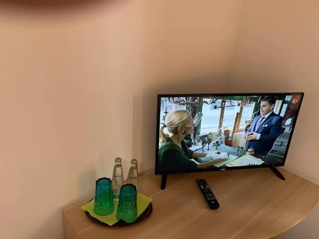 A television on a wooden table with a remote control, a glass of water, and a bottle of water.