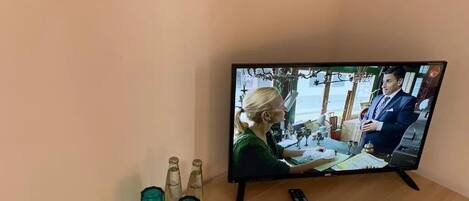 Un televisor sobre una mesa de madera, con un control remoto, un vaso de agua y una botella de agua.