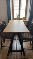 Uma mesa de jantar com duas cadeiras, uma janela com cortinas e duas plantas em vasos no parapeito.