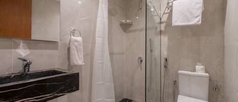 A modern bathroom with a glass-enclosed shower, a black marble sink, a white toilet, and a towel rack.