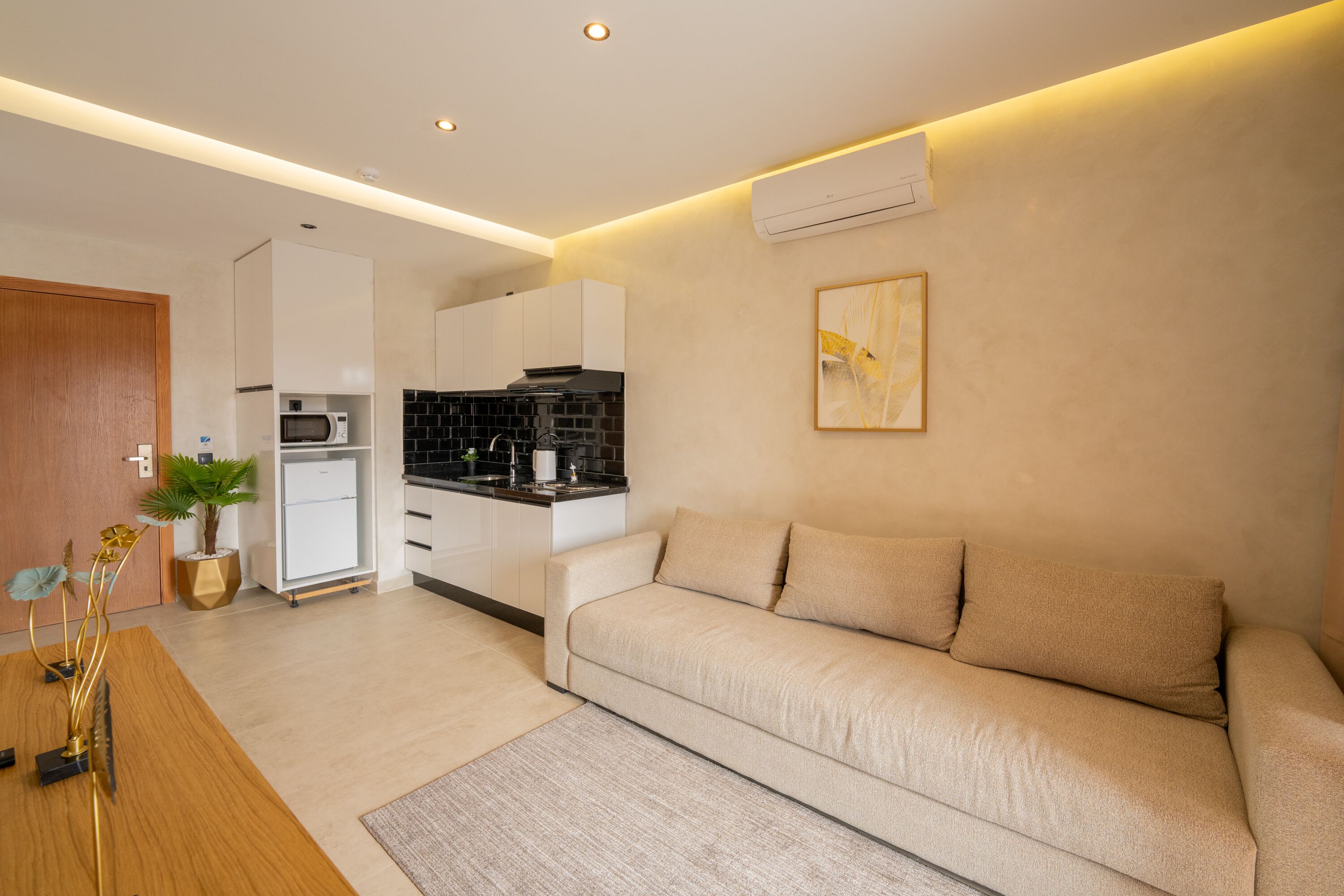 A modern living room with a sofa, a dining table with a plant, and a kitchen in the background.