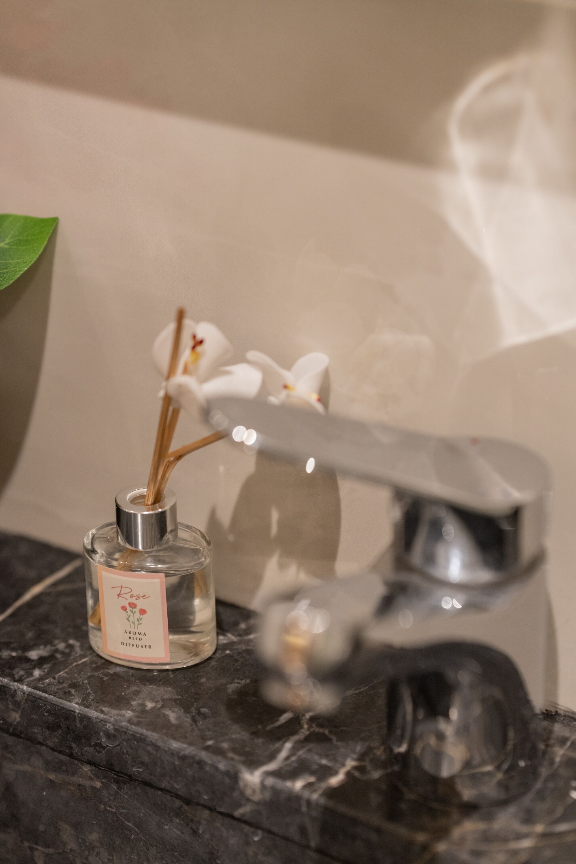 Une salle de bain avec un lavabo en marbre, un flacon de diffuseur aux senteurs de rose et une orchidée blanche.