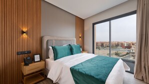 Quarto de hotel moderno com uma cama grande, uma mesa de cabeceira com telefone e vista da cidade através de uma janela ampla.