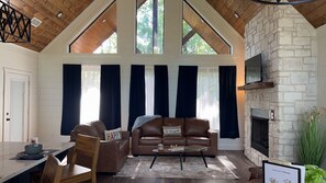 Ein geräumiges Wohnzimmer mit Kamin aus Stein, einem braunen Ledersofa und einem Essbereich mit Tisch und Stühlen.
