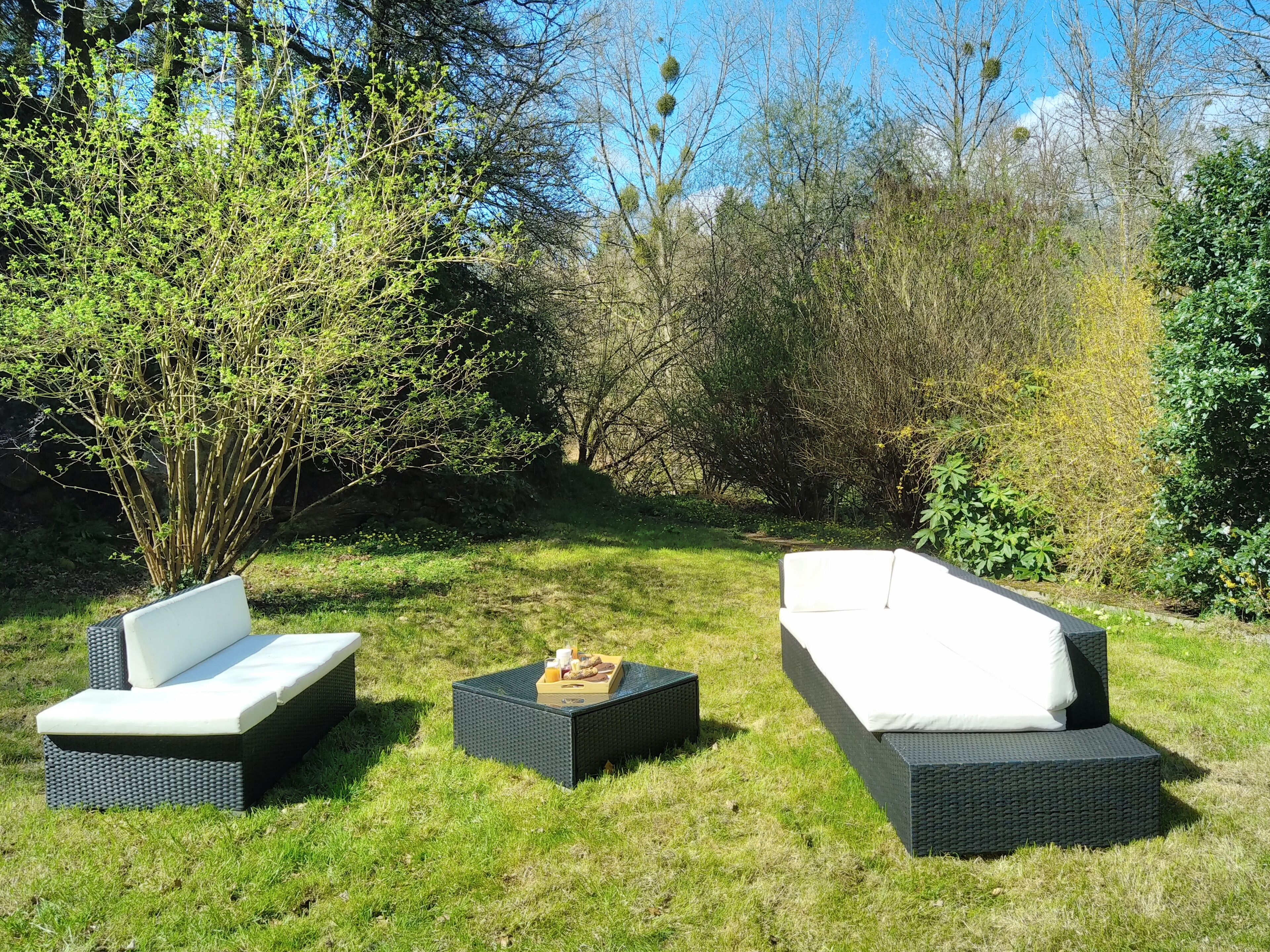 Un jardin agrémenté de deux canapés d’extérieur et d’une table, le tout entouré de verdure et d’arbres.