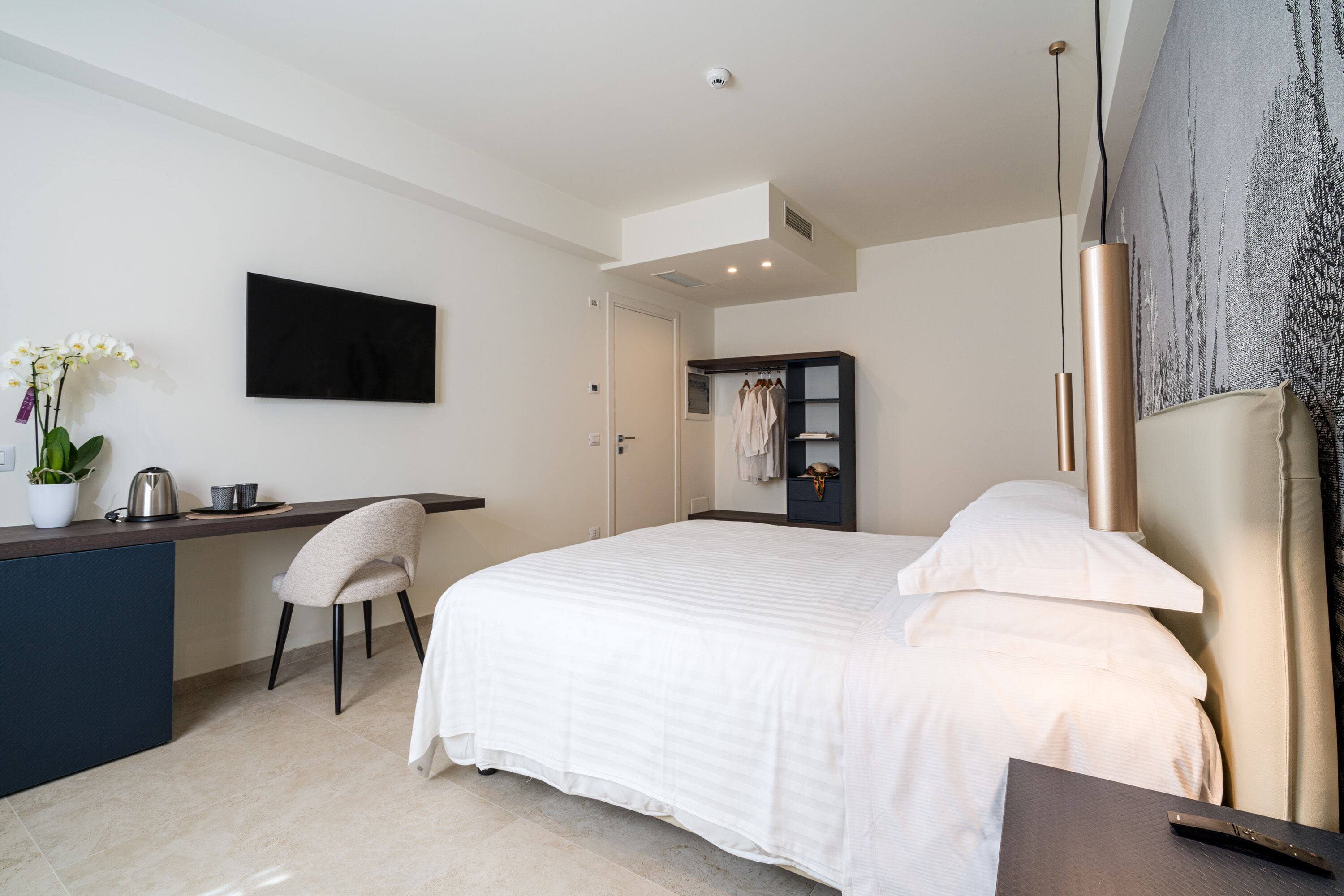 Una camera d'albergo moderna con un letto grande, una scrivania con una sedia, una pianta in vaso e un quadro appeso al muro.