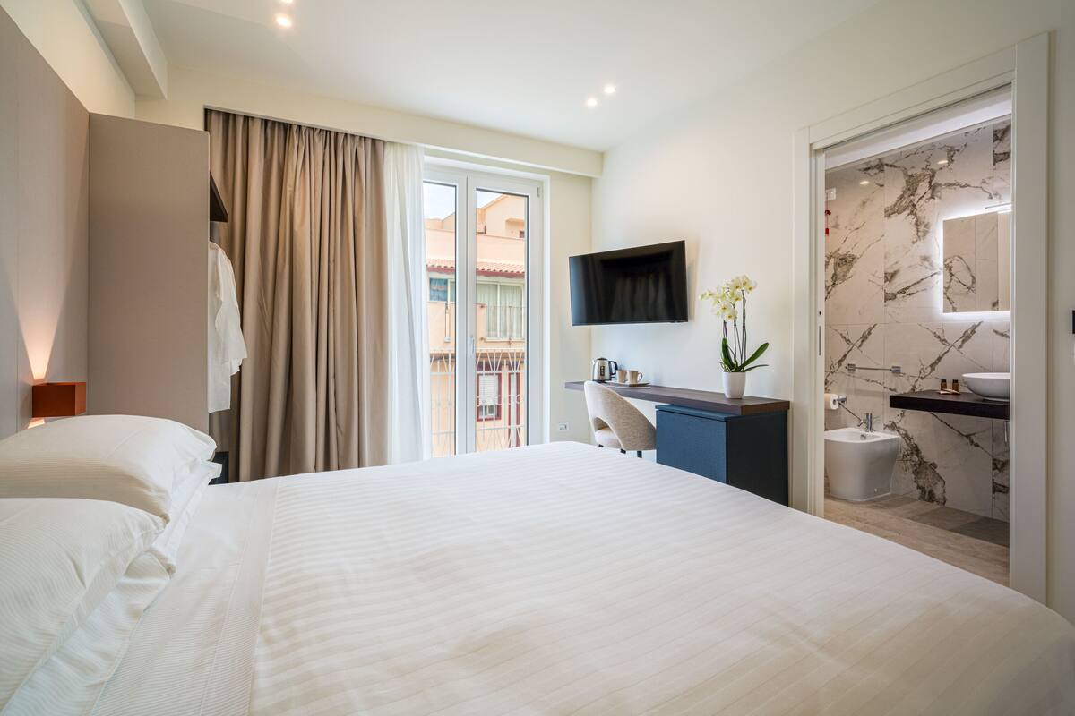 Een hotelkamer met een groot bed, een bureau, een televisie en een badkamer met een marmeren wand.
