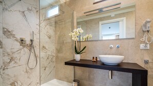 A modern bathroom with a marble wall, a glass shower enclosure, a white sink, and a potted orchid.