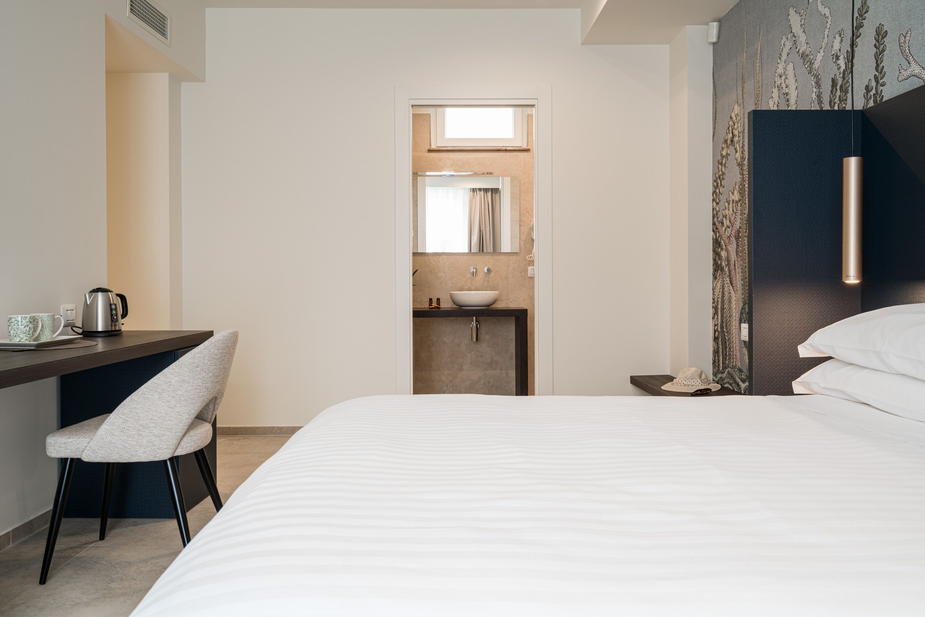Una habitación de hotel con una cama, un escritorio con silla, un lavamanos y una mesita de noche.