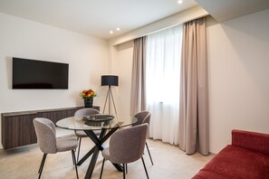 Un comedor moderno con una mesa de vidrio, cuatro sillas, un televisor de pantalla plana en la pared, una lámpara y un sofá rojo.