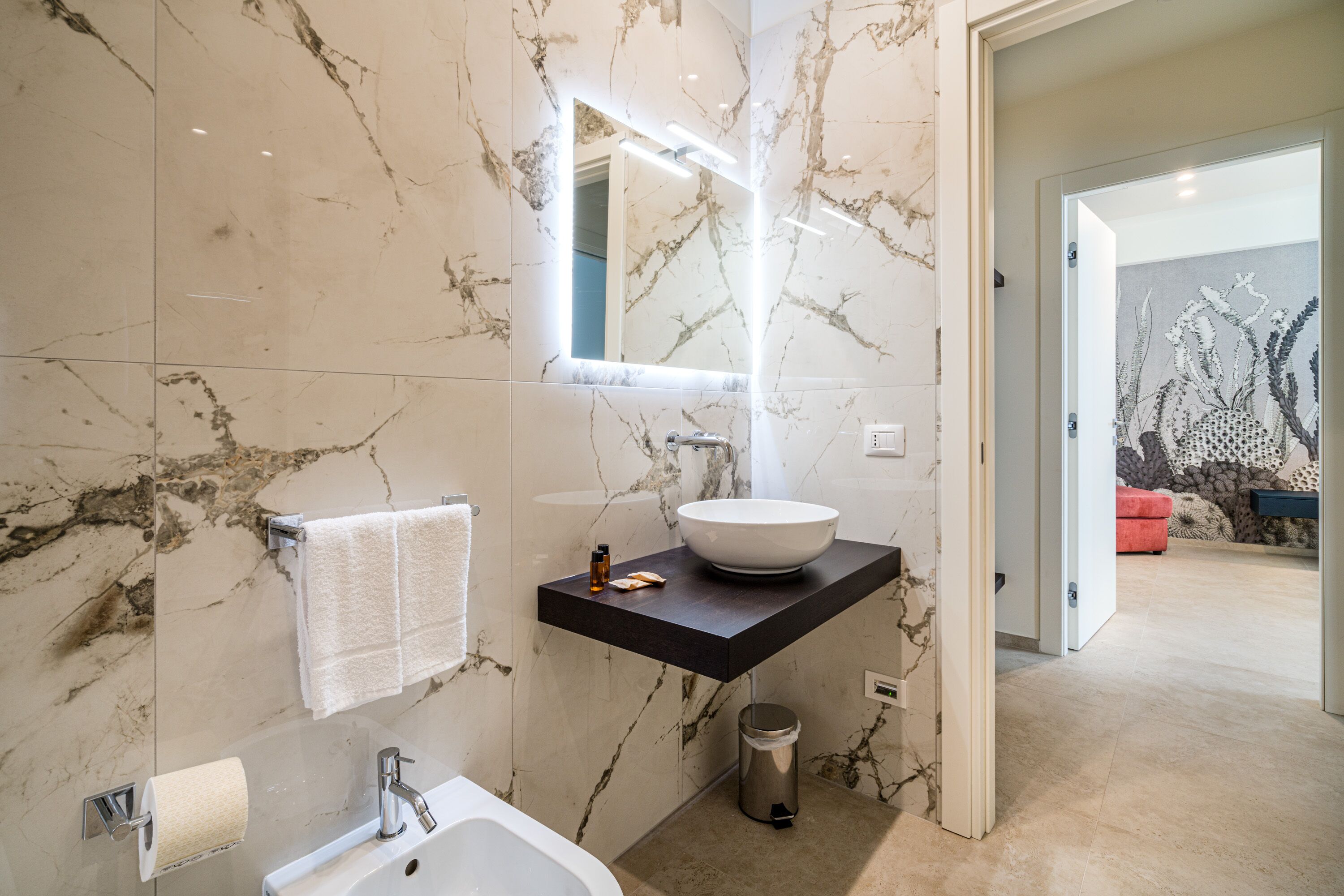 Un baño moderno con salpicadero de mármol, un espejo grande, un lavabo sobre encimera y un inodoro.