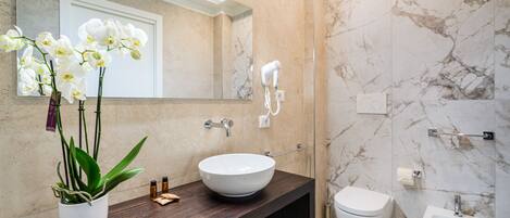 A modern bathroom with a marble wall, a white sink, a bidet, and a hairdryer mounted on the wall.