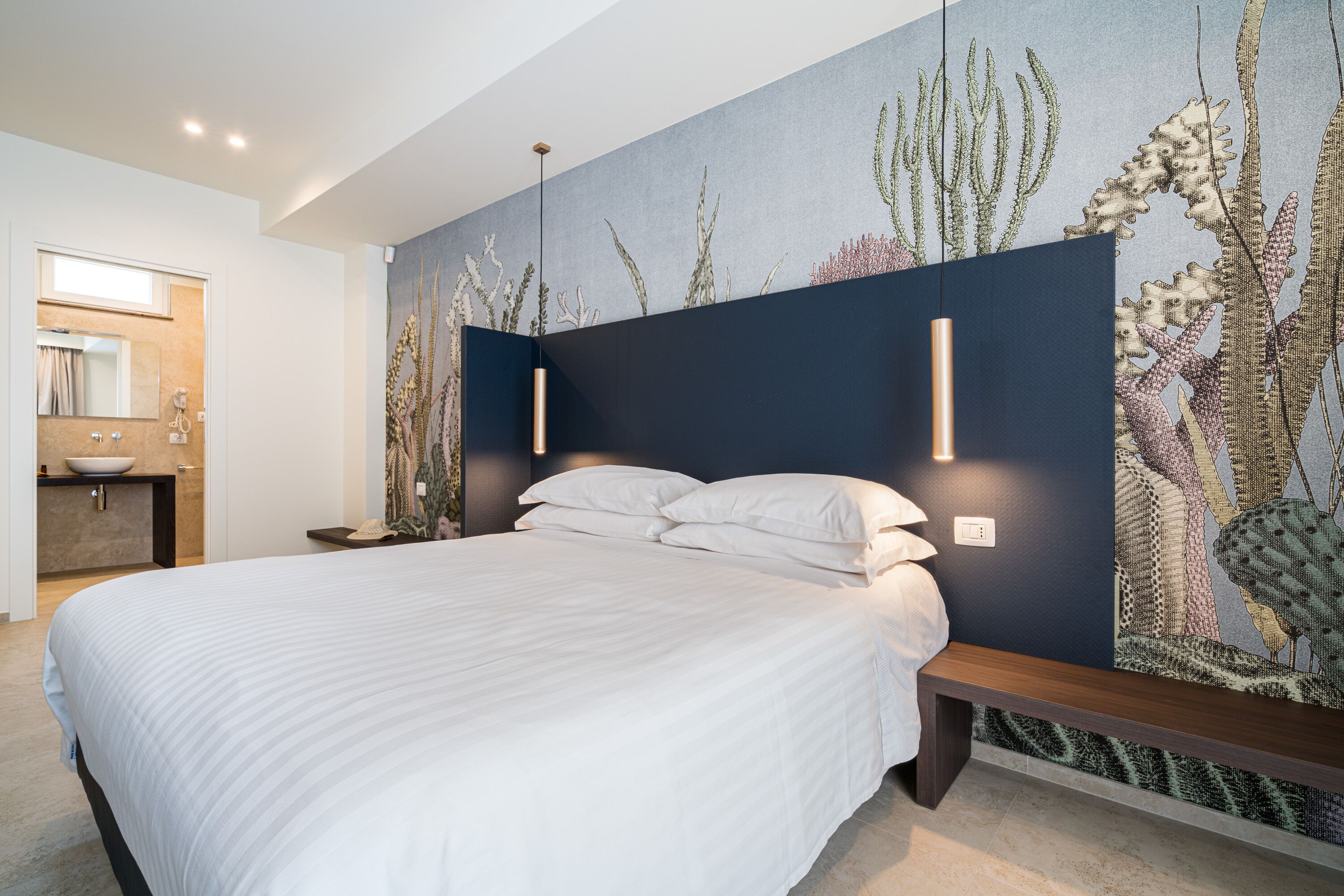 Une chambre moderne avec un grand lit, un banc intégré et une fresque murale représentant des plantes marines.