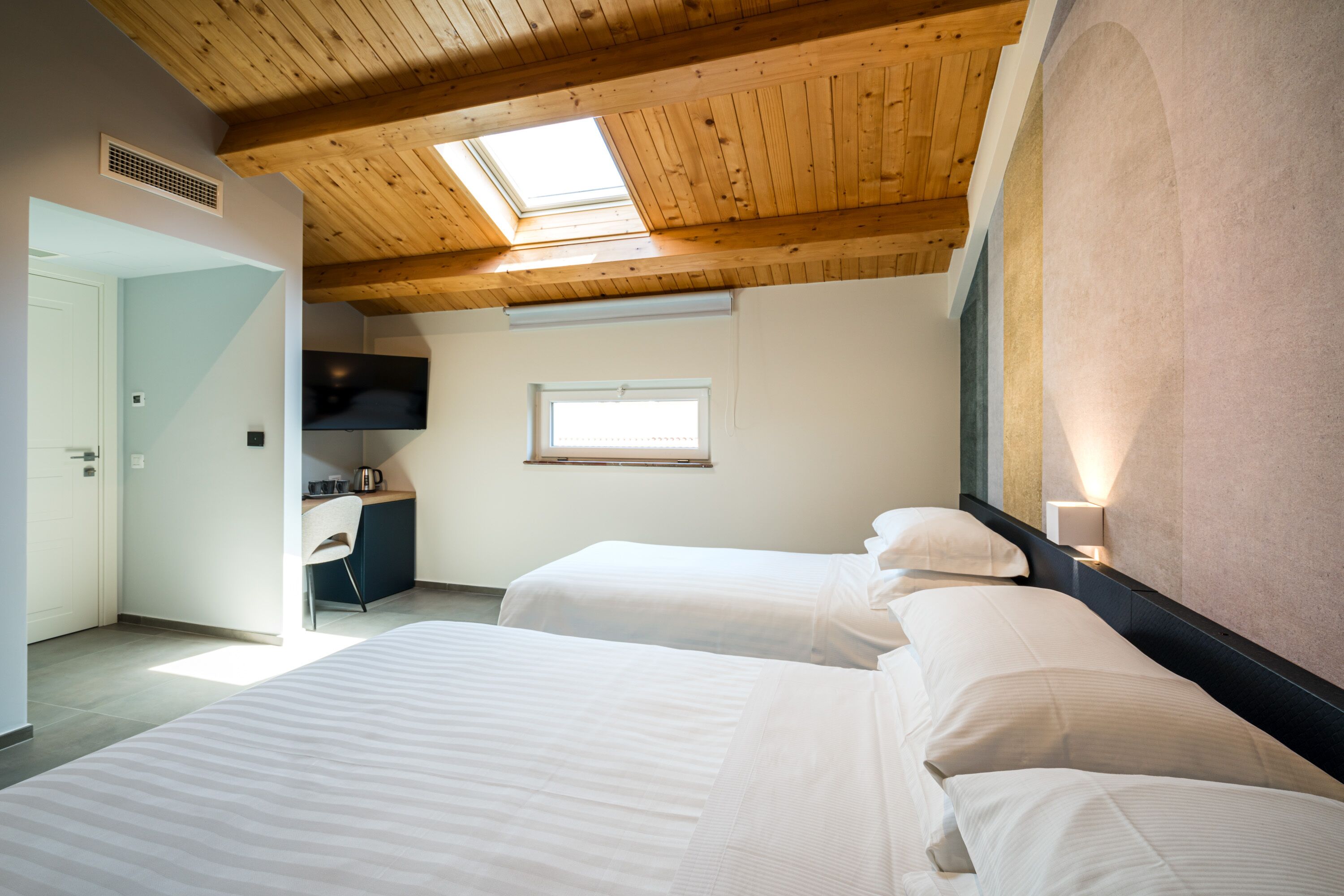 A bedroom with two beds, a skylight, a desk, and a window.