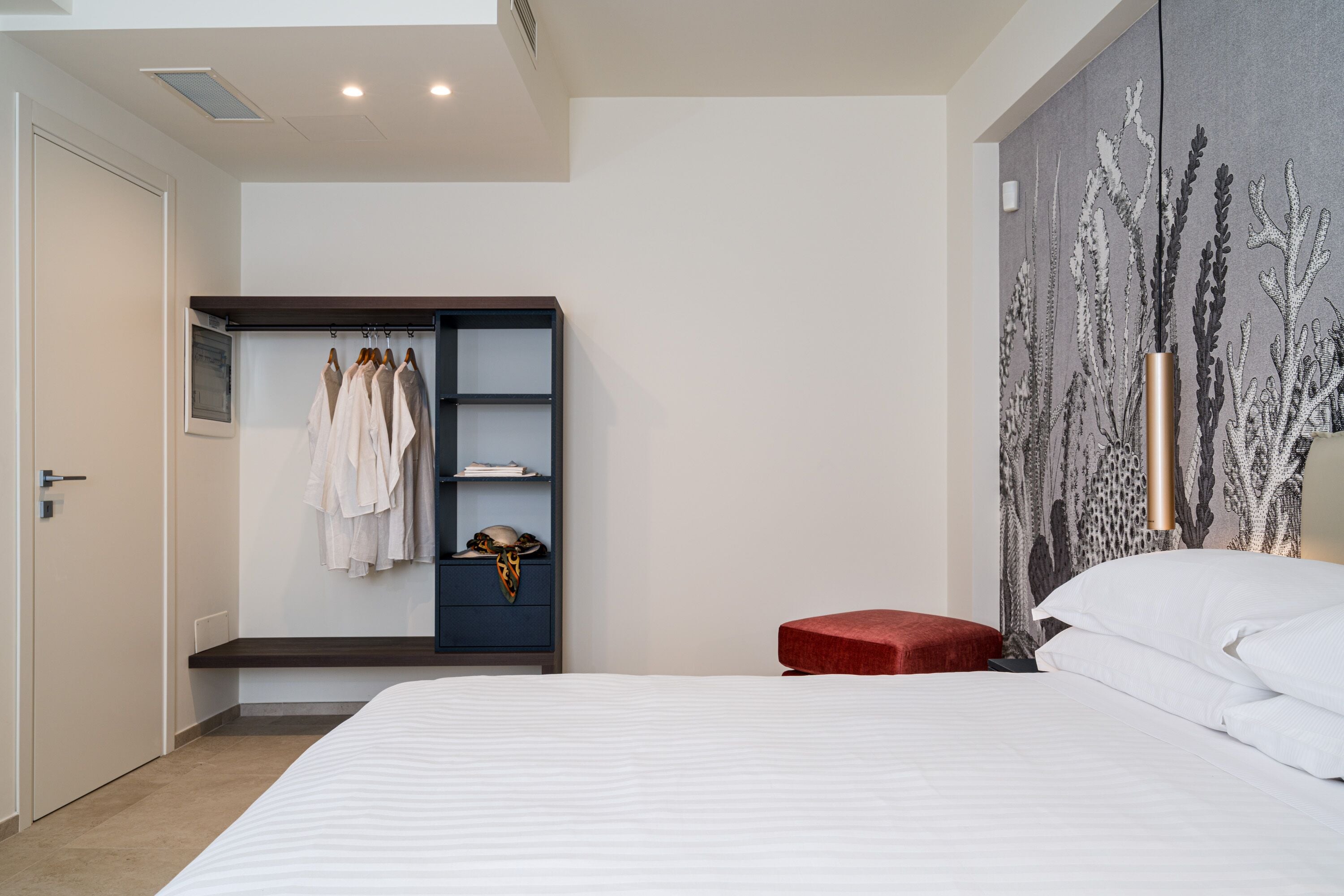 A bedroom with a bed, a wardrobe, a red bench, and a wall with a plant design.