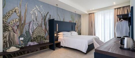 A modern hotel room with a large mural of marine life on the wall, a bed with a dark headboard, a bedside table, and a view of the city through large windows.