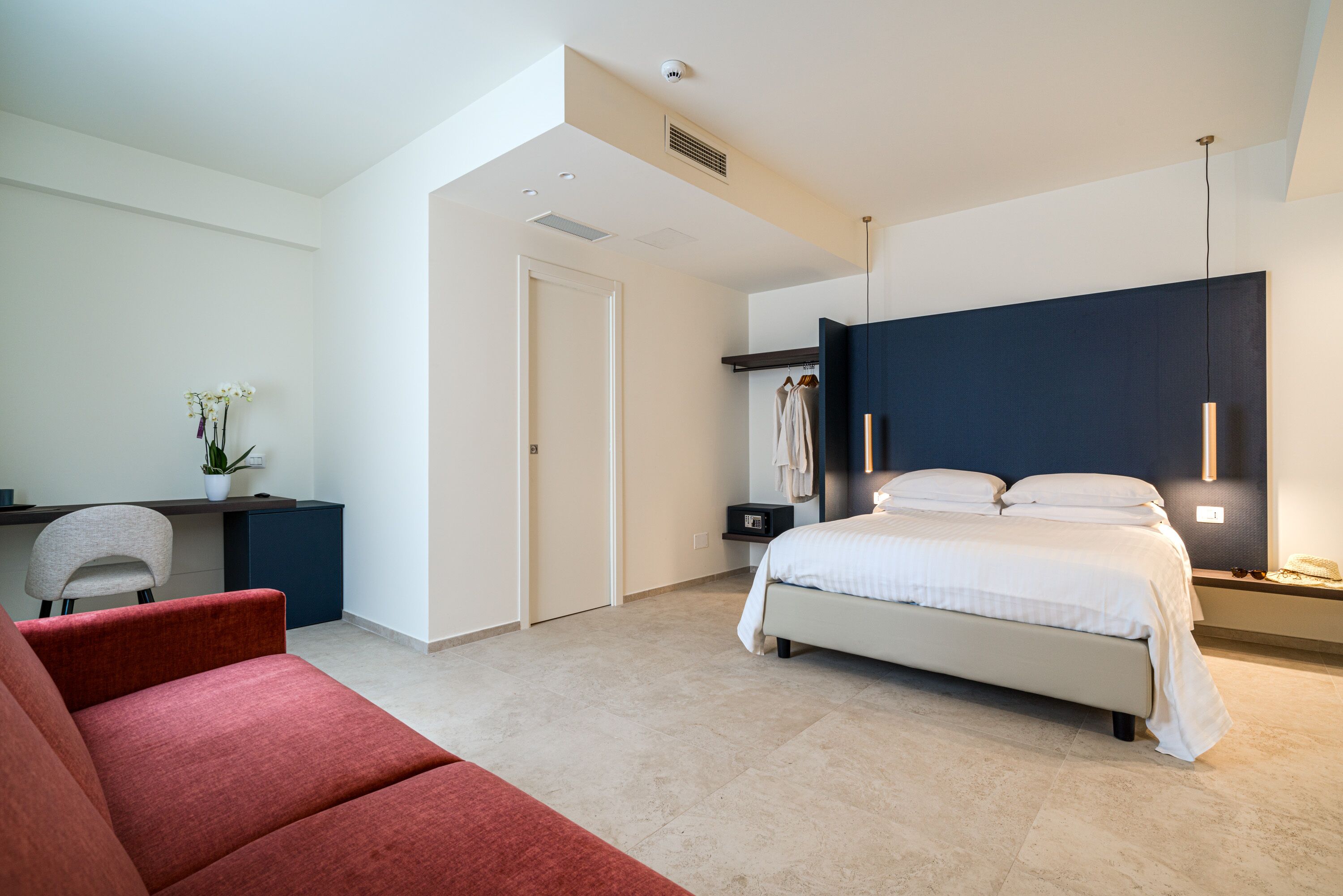 A modern bedroom with a bed, a desk, a chair, and a red sofa.