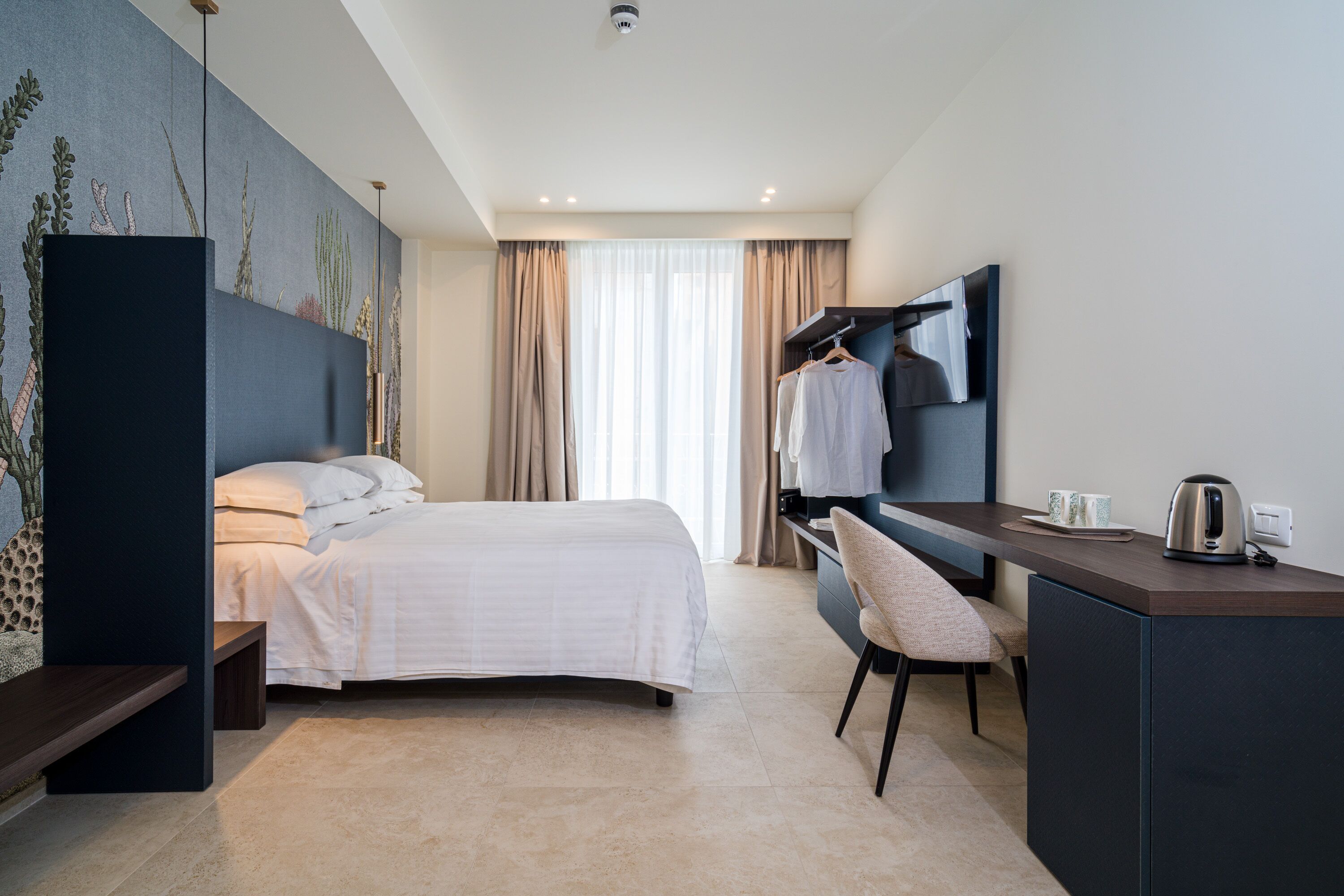 A hotel room with a bed, a desk, a chair, a TV, and a window with curtains.