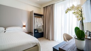 A hotel room with a bed, a desk, a chair, a wardrobe, and a potted orchid.