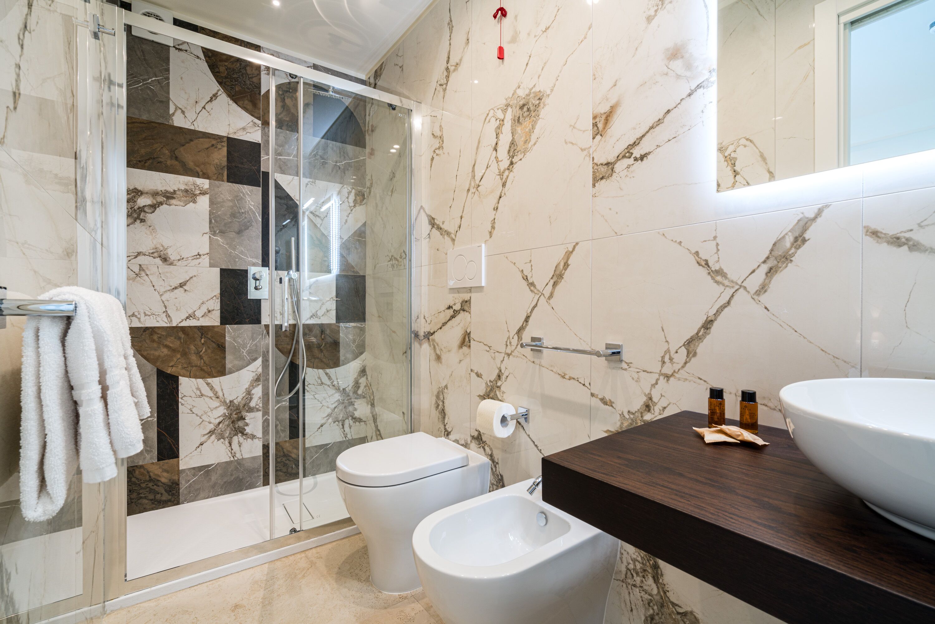 A modern bathroom with a glass shower enclosure, a toilet, a bidet, and a large sink with a dark countertop.