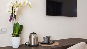A modern room with a wooden desk, a potted orchid, a kettle, and a flat-screen TV.