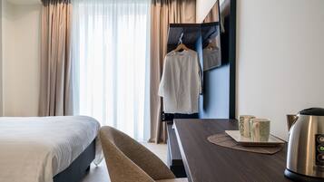 Ein Hotelzimmer mit einem Bett, einem Holztisch mit Wasserkocher und zwei Tassen, einem Sessel und einem Kleiderschrank mit Spiegel.