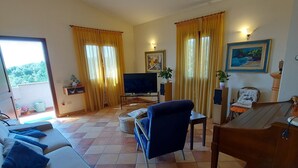 A living room with a sofa, a TV, a piano, and a dining table. - Agriturismo Podere Pilar (Monsummano Terme)