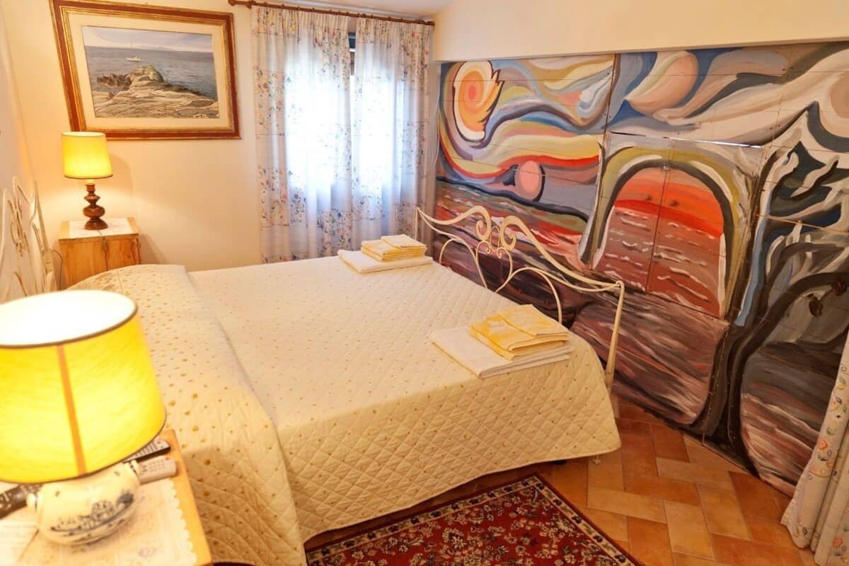 Een slaapkamer met een bed, een lamp, een schilderij en een vloerkleed.