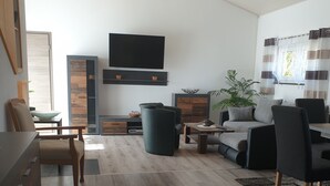 A modern living room with a sofa, chairs, a coffee table, and a TV mounted on the wall. - Appartement mit gr. Garten u. 2 Bäder (Vilshofen an der Donau)