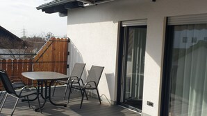 A covered outdoor area with a table and chairs, a sliding glass door, and a wooden deck. - Appartement mit gr. Garten u. 2 Bäder (Vilshofen an der Donau)