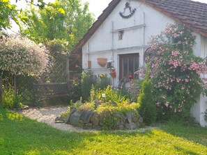 Un bâtiment blanc doté d’un toit en pente, entouré d’un jardin où poussent différentes plantes et fleurs.